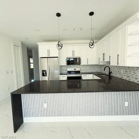 Kitchen featuring open shelves, dark stone counters, decorative backsplash, stainless steel appliances, and white cabinets