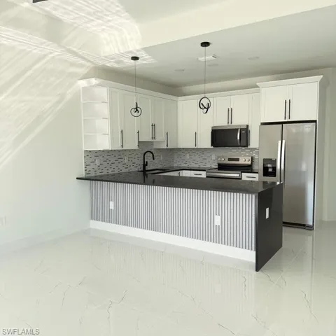 Kitchen featuring backsplash, stainless steel appliances, white cabinetry, and a peninsula