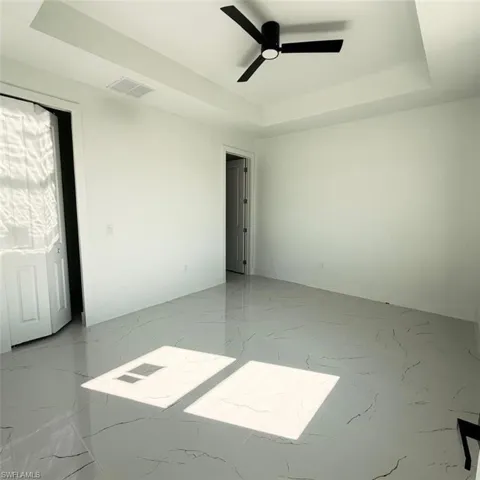 Empty room with a raised ceiling, ceiling fan, and light marble finish flooring