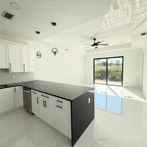 Kitchen with pendant lighting, light marble finish flooring, white cabinetry, open floor plan, and dark stone countertops