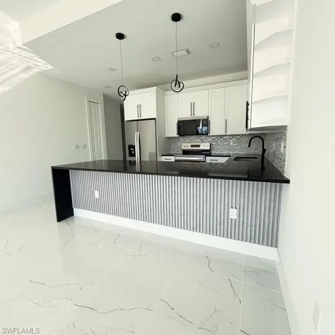 Kitchen with open shelves, stainless steel appliances, decorative backsplash, light marble finish floors, and white cabinetry