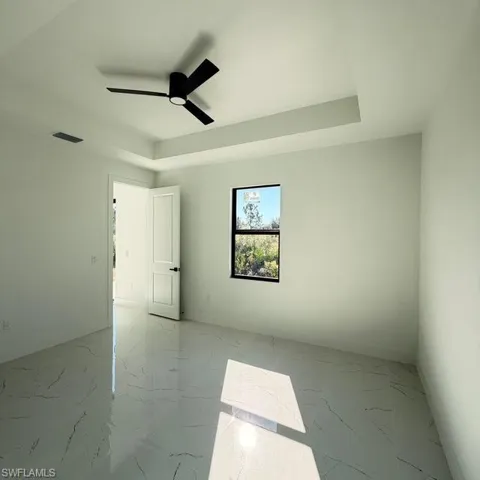 Unfurnished room with light marble finish flooring, a raised ceiling, and a ceiling fan
