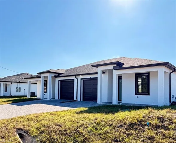 Prairie-style home with an attached garage, decorative driveway, a front yard, stucco siding, and roof with shingles