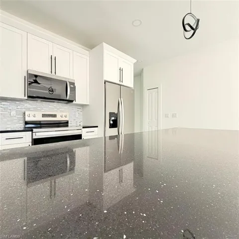 Kitchen featuring stainless steel appliances, white cabinetry, decorative backsplash, and dark stone counters