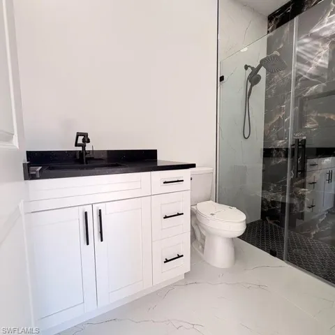 Bathroom featuring vanity, a marble finish shower, and light marble finish floors