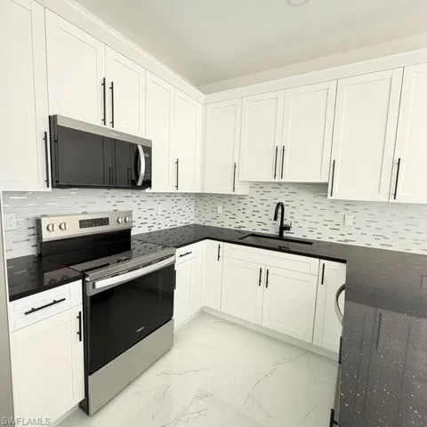 Kitchen featuring stainless steel appliances, white cabinets, and light marble finish floors
