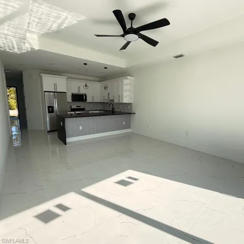Kitchen with open floor plan, stainless steel appliances, white cabinets, ceiling fan, and a peninsula