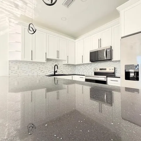 Kitchen with decorative light fixtures, white cabinets, stainless steel appliances, and dark stone countertops