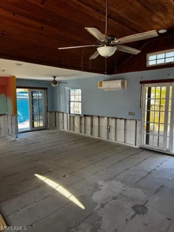 Unfurnished room featuring high vaulted ceiling, an AC wall unit, wooden ceiling, and a ceiling fan