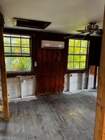 Unfurnished living room featuring hardwood / wood-style floors, a wall unit AC, a ceiling fan, and plenty of natural light