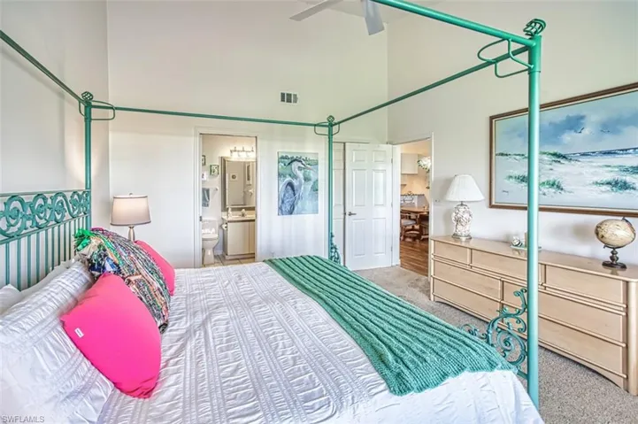Carpeted bedroom featuring high vaulted ceiling, ensuite bath, and ceiling fan