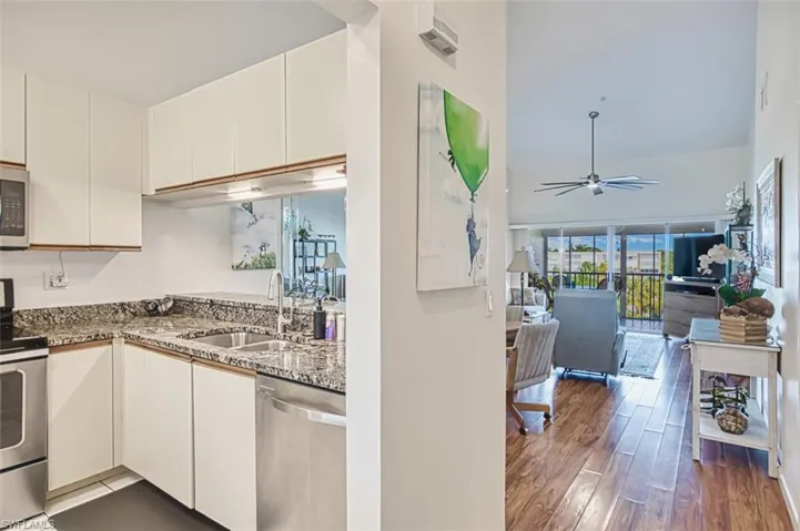 Kitchen with appliances with stainless steel finishes, ceiling fan, dark stone countertops, wood finished floors, and white cabinetry