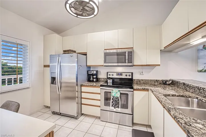 Kitchen with appliances with stainless steel finishes, vaulted ceiling, light tile patterned floors, white cabinets, and dark countertops