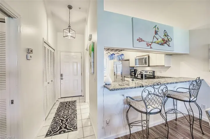 Kitchen with stainless steel appliances, a breakfast bar area, light tile patterned flooring, white cabinets, and decorative light fixtures