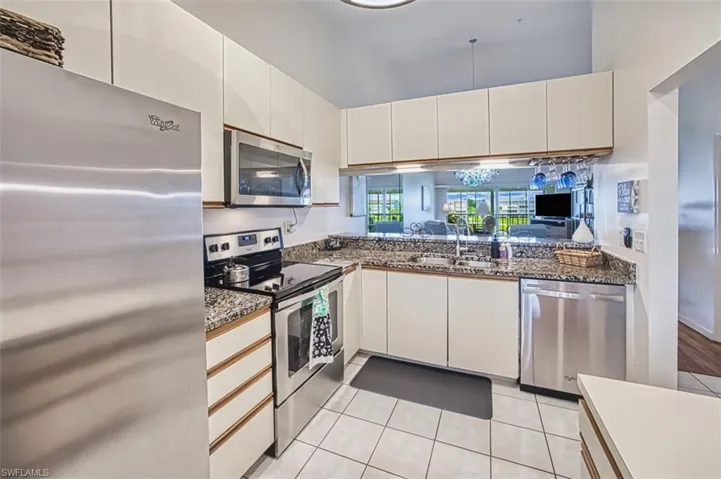 Kitchen featuring appliances with stainless steel finishes, light tile patterned floors, white cabinetry, and dark stone countertops