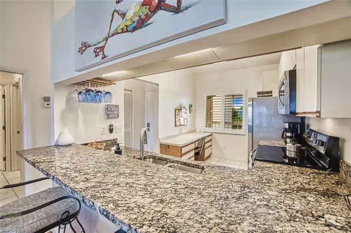 Kitchen featuring stove, light stone counters, a peninsula, light tile patterned floors, and stainless steel microwave