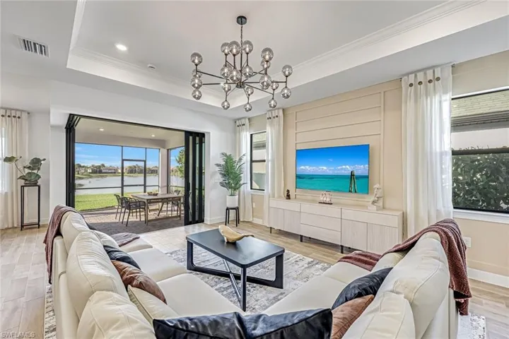 Living area featuring light wood-style floors, ornamental molding, recessed lighting, a chandelier, and a tray ceiling