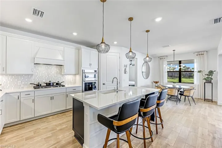 Kitchen with hanging light fixtures, light wood-style flooring, white cabinets, and recessed lighting
