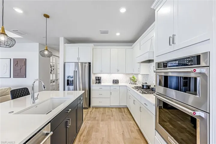 Kitchen with stainless steel appliances, white cabinetry, pendant lighting, light stone countertops, and custom range hood