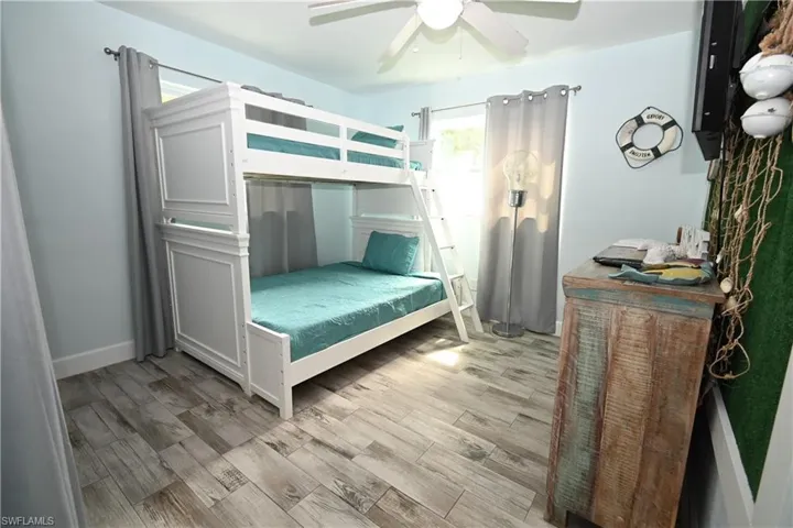 White bunk bed with a ladder, wood-finish flooring, light blue walls, and a ceiling fan