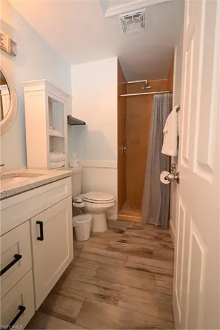 Bathroom featuring wood-finish flooring, a white vanity with black hardware, a shower with a wood-look surround, and a built-in shelving unit