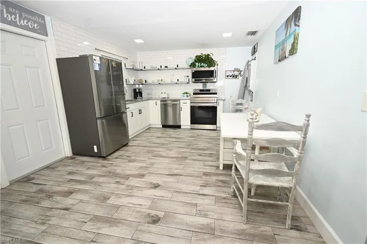 Kitchen featuring wood-finish tile flooring, white shaker cabinetry, stainless steel appliances, and a subway tile backsplash