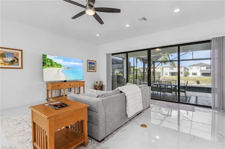 Open living area featuring a ceiling fan, recessed lighting, and marble finish floors looking out to the screened in lanai