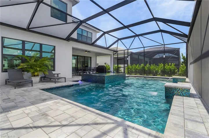 Private oasis—a custom-designed oversized pool with 360° tile waterfall spa, dual tile waterfall features, splash pads, and relaxing water benches, all enclosed in a screened-in lanai with super screen, picture window, and ambient lanai lighting.