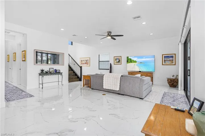 Open living room with light marble finish flooring, recessed lighting, ceiling fan, and stairway
