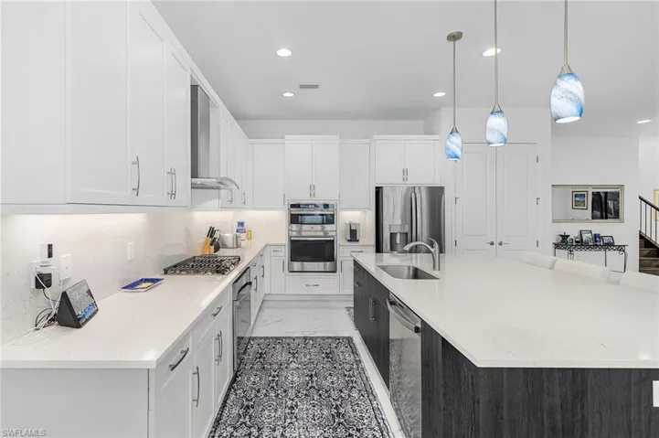 Gourmet kitchen featuring under cabinet lighting, upgraded appliances with stainless steel finishes, white cabinets, a spacious island, and pendant lighting
