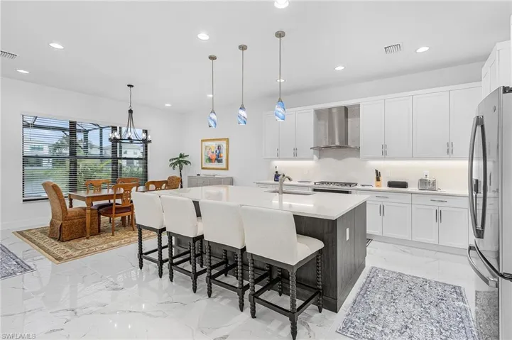 Gourmet kitchen with freestanding refrigerator, recessed lighting, light marble finish floors, backsplash, and wall chimney range hood