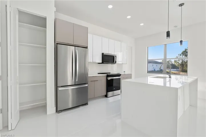 Dual tone kitchen featuring stainless steel appliances, hanging light fixtures, modern cabinets, light stone counters, and a center island with sink