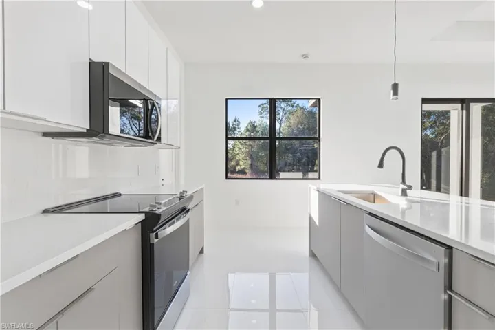 Kitchen with stainless steel appliances, modern cabinets, hanging light fixtures, light stone counters, and light tile patterned floors