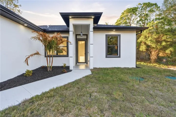 Exterior entry at dusk with a yard and stucco siding