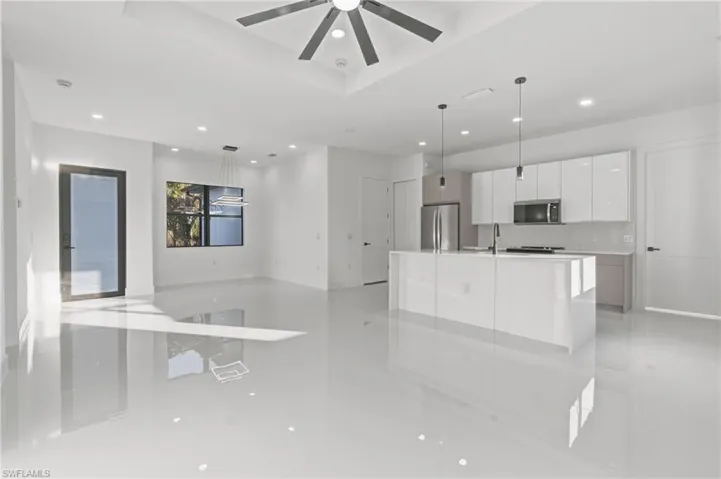 Kitchen with white cabinetry, open floor plan, hanging light fixtures, a center island with sink, and modern cabinets