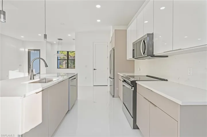 Kitchen featuring modern cabinets, stainless steel appliances, decorative light fixtures, white cabinetry, and a kitchen island with sink