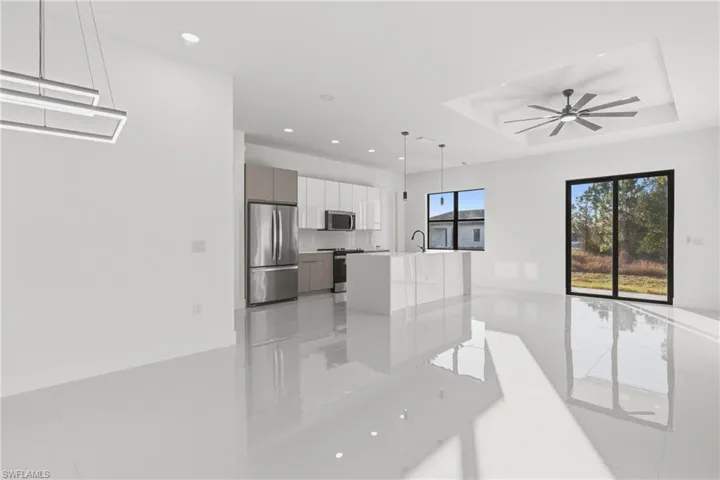 Kitchen with stainless steel appliances, hanging light fixtures, modern cabinets, white cabinets, and a kitchen island with sink