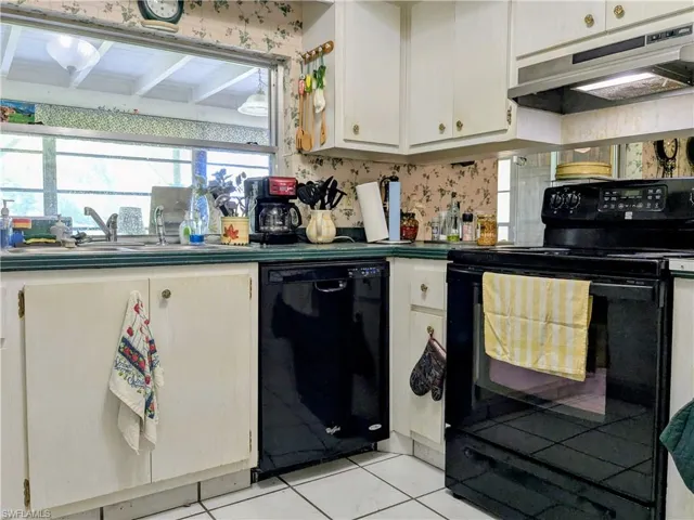Kitchen with black appliances, under cabinet range hood, white cabinets, light tile patterned flooring, and plenty of natural light