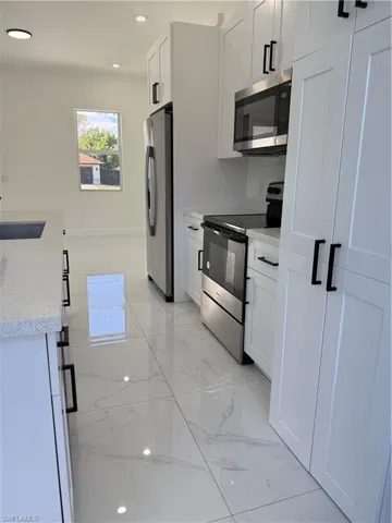Kitchen featuring light marble finish floors, stove, fridge, light stone counters, and white cabinets