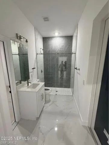 Full bath with a shower stall, vanity, and light marble finish flooring