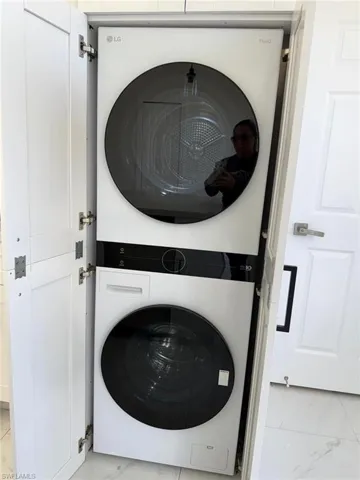 Laundry room featuring stacked washer / drying machine and light marble finish flooring
