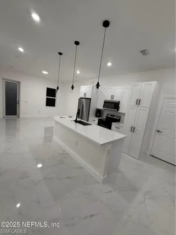 Kitchen with an island with sink, decorative light fixtures, recessed lighting, appliances with stainless steel finishes, and white cabinetry