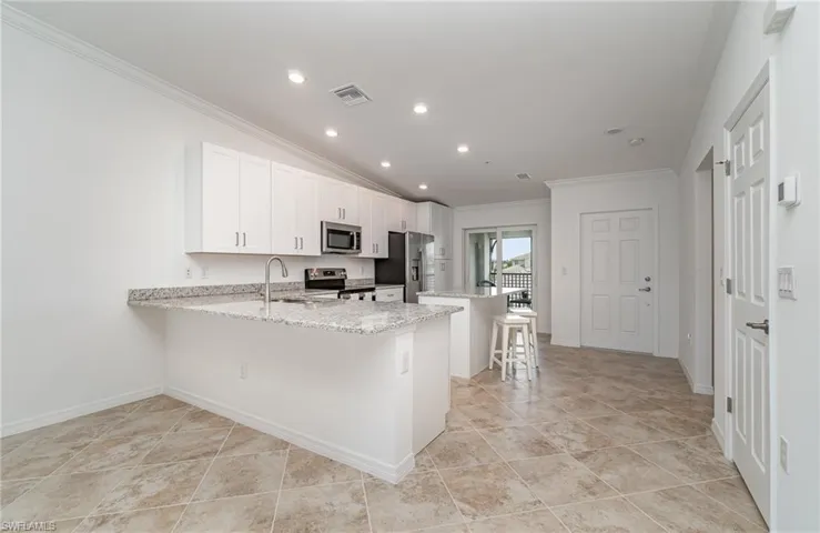 Kitchen featuring stainless steel appliances, ornamental molding, light stone counters, lofted ceiling, and light tile patterned floors