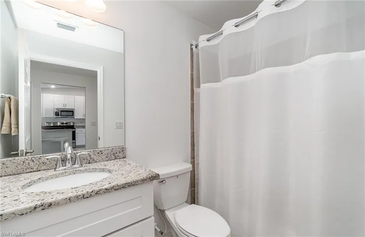 Bathroom with toilet, a shower with shower curtain, and vanity