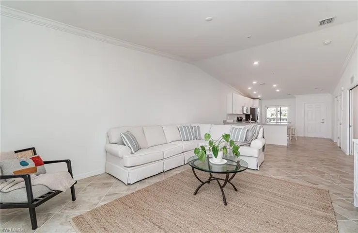 Living room featuring vaulted ceiling, light tile patterned flooring, and ornamental molding