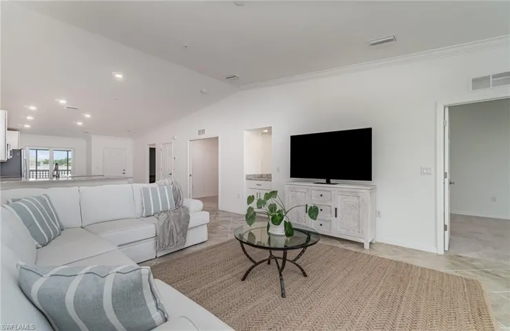 Living room with light tile patterned floors, vaulted ceiling, and ornamental molding