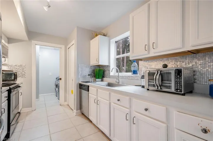 Kitchen with stainless steel appliances, sink, tasteful backsplash, light tile patterned flooring, and white cabinetry