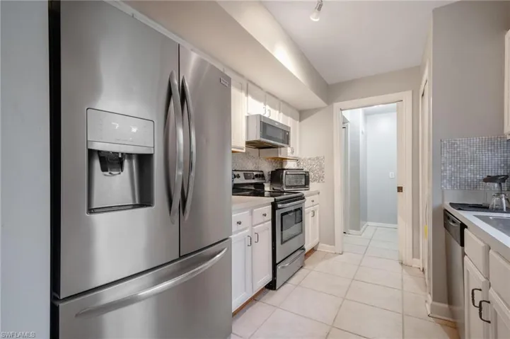 Kitchen featuring white cabinetry, backsplash, appliances with stainless steel finishes, and light tile patterned flooring