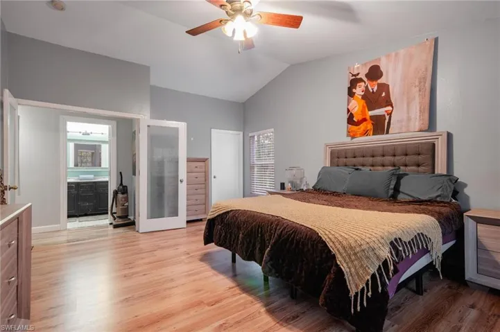 Bedroom featuring light hardwood / wood-style floors, ceiling fan, ensuite bath, and vaulted ceiling