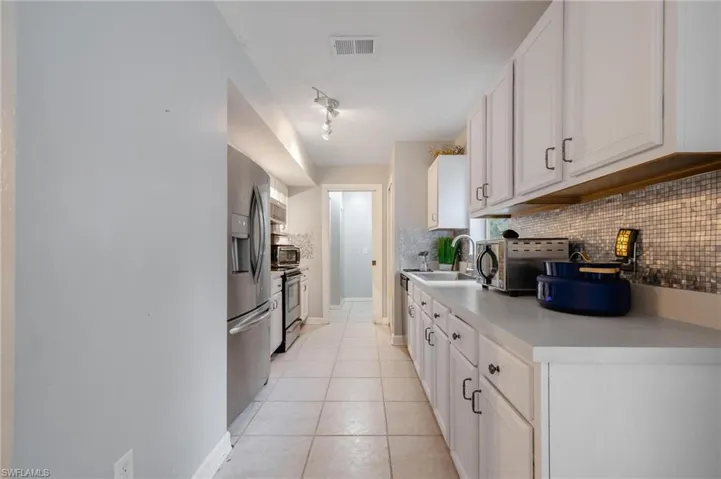 Kitchen with light tile patterned flooring, sink, appliances with stainless steel finishes, white cabinets, and decorative backsplash